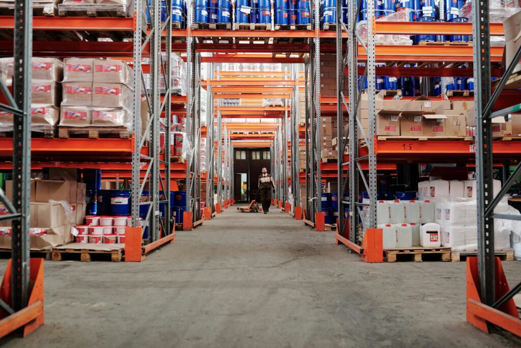 A spacious industrial warehouse with stocked shelves and a worker in protective gear.