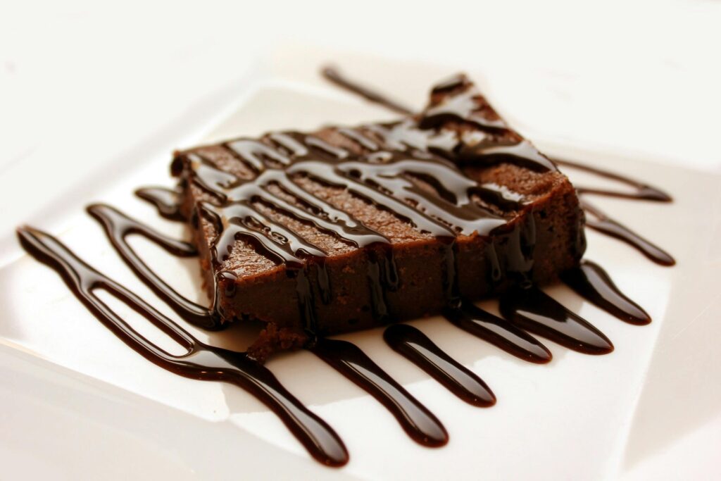 Rich chocolate brownie drizzled with syrup on a clean white plate, perfect for dessert lovers.